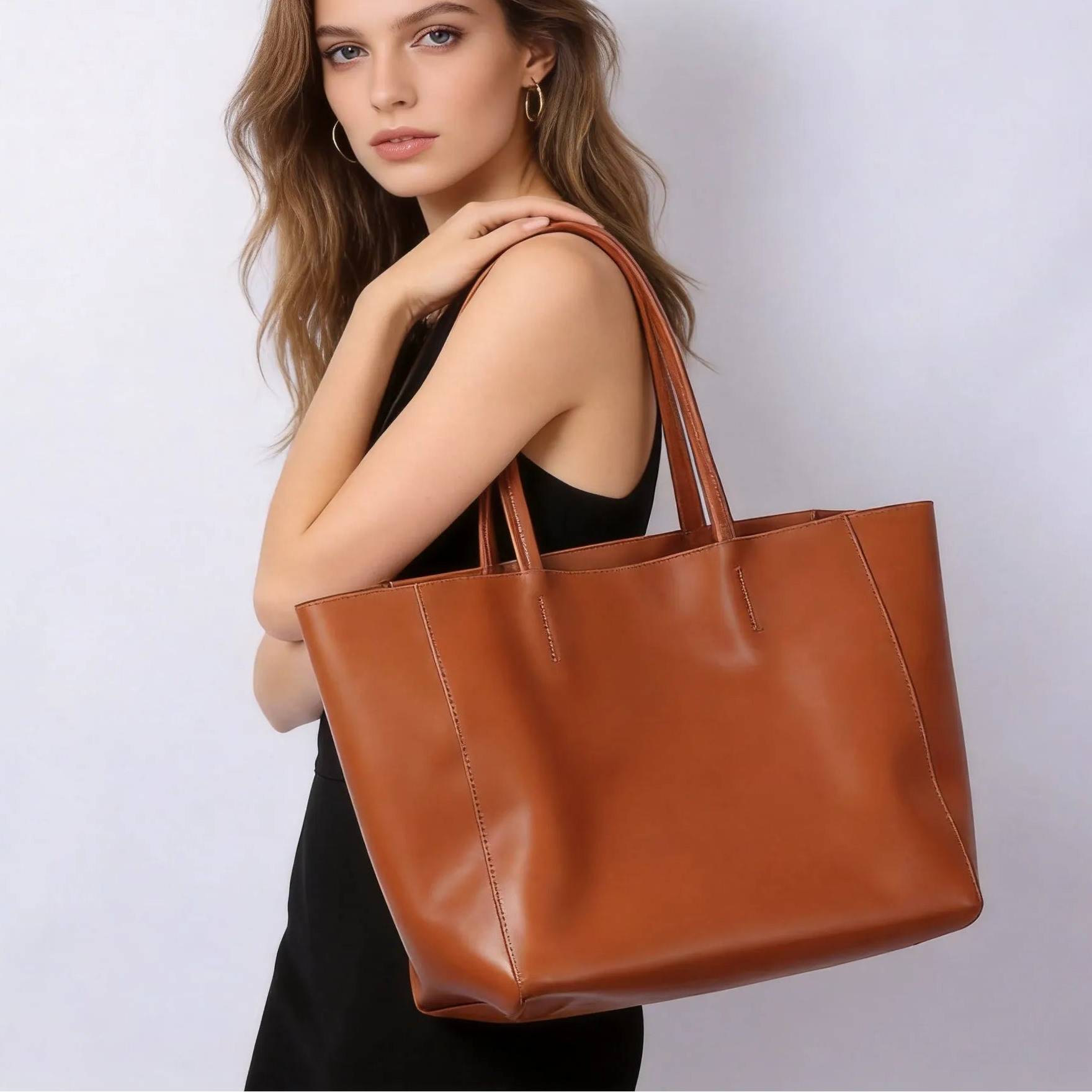 Woman holding a brown leather tote bag against a plain background