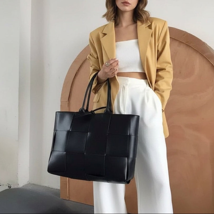 Woman holding a black woven handbag against a neutral background