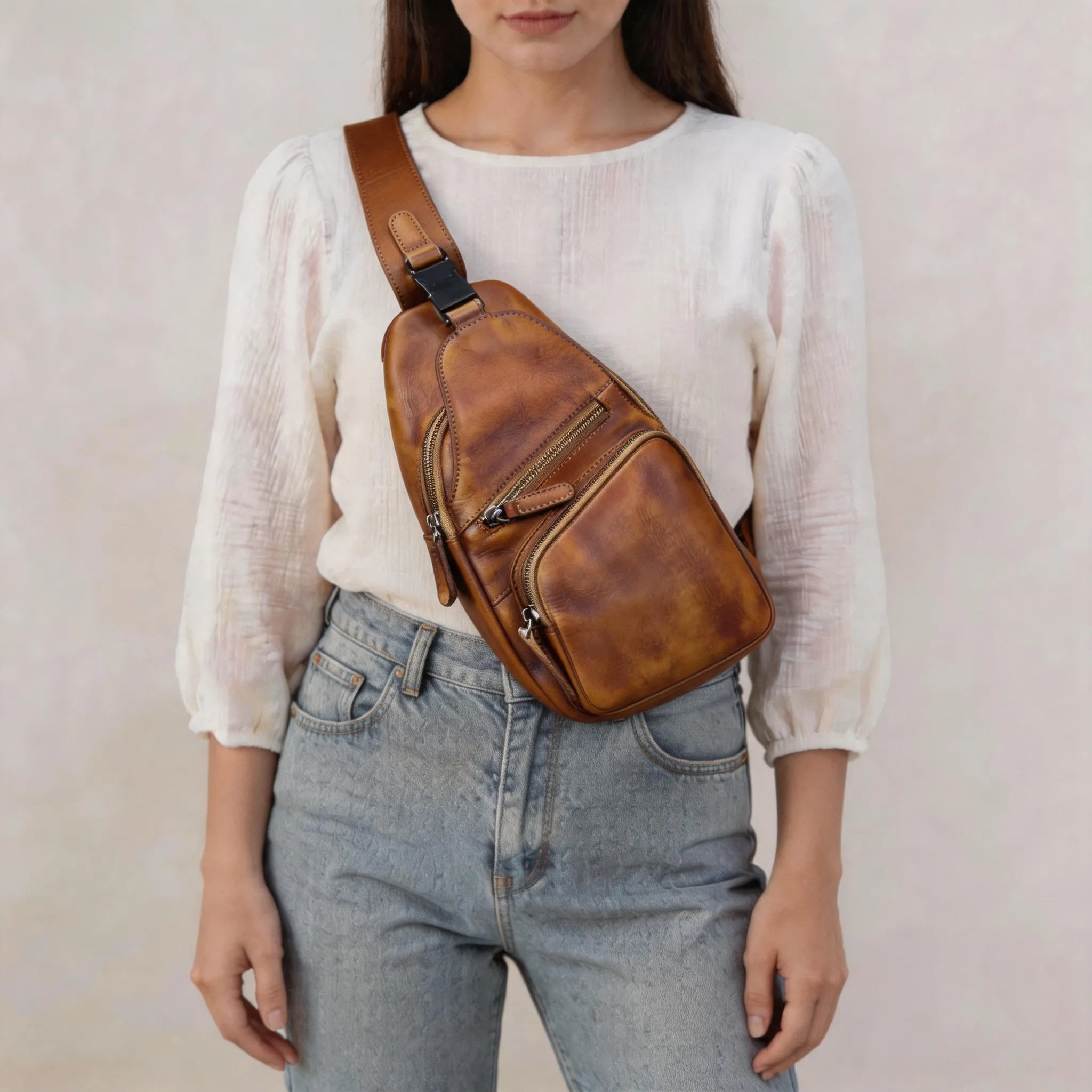 Person wearing a brown leather sling bag over one shoulder against a plain background