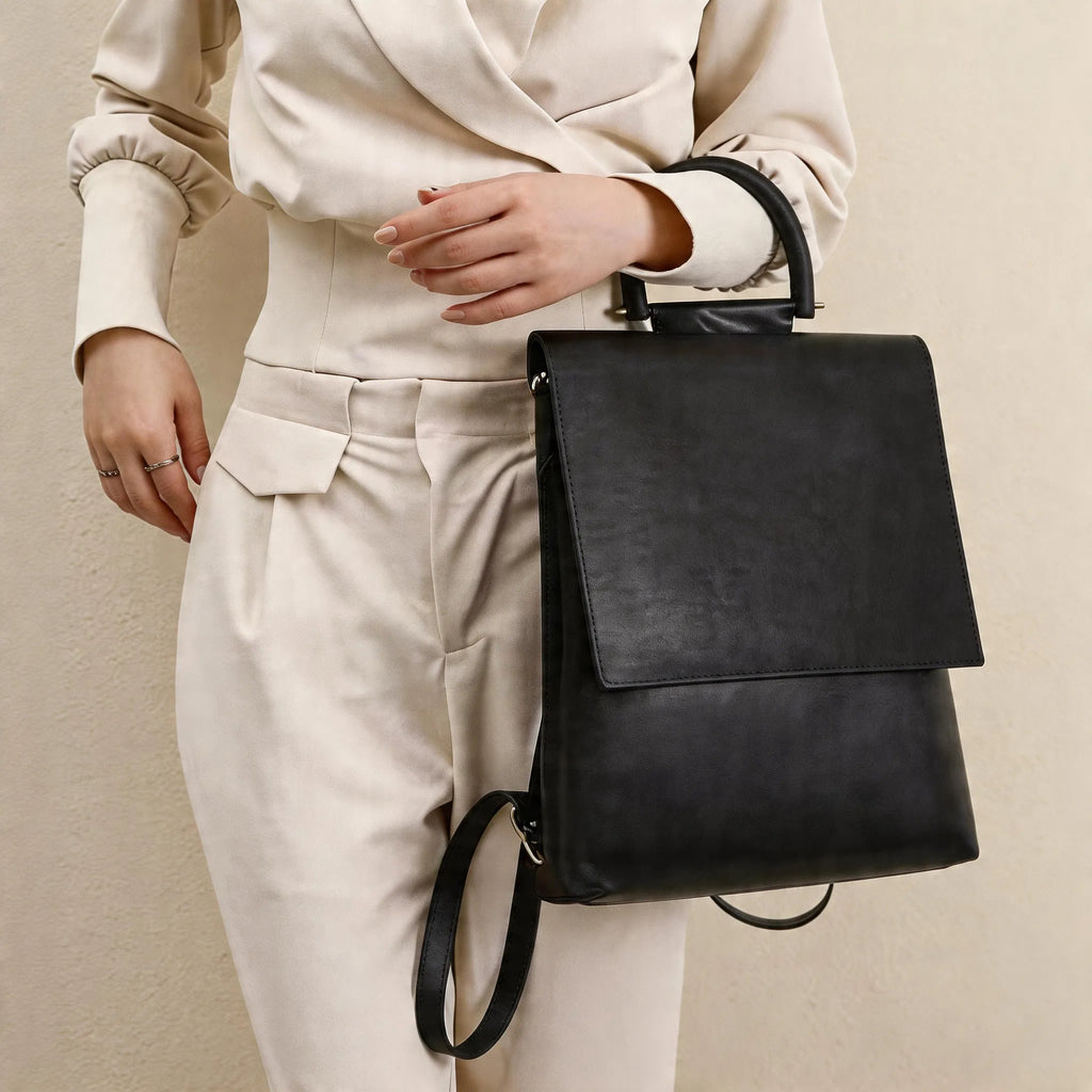 Person holding a black leather backpack against a neutral background