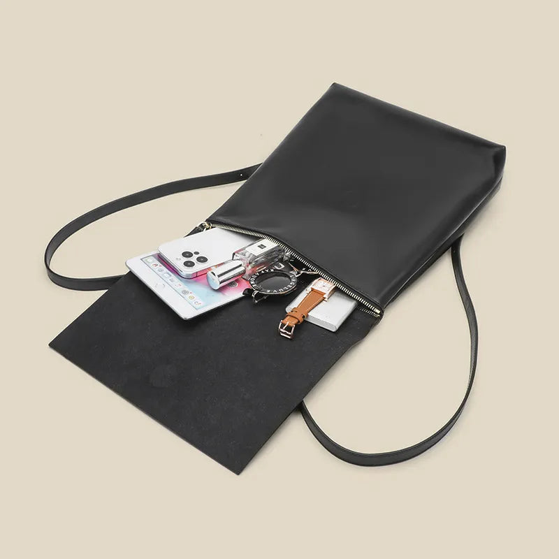 Black crossbody bag with items inside on a beige background