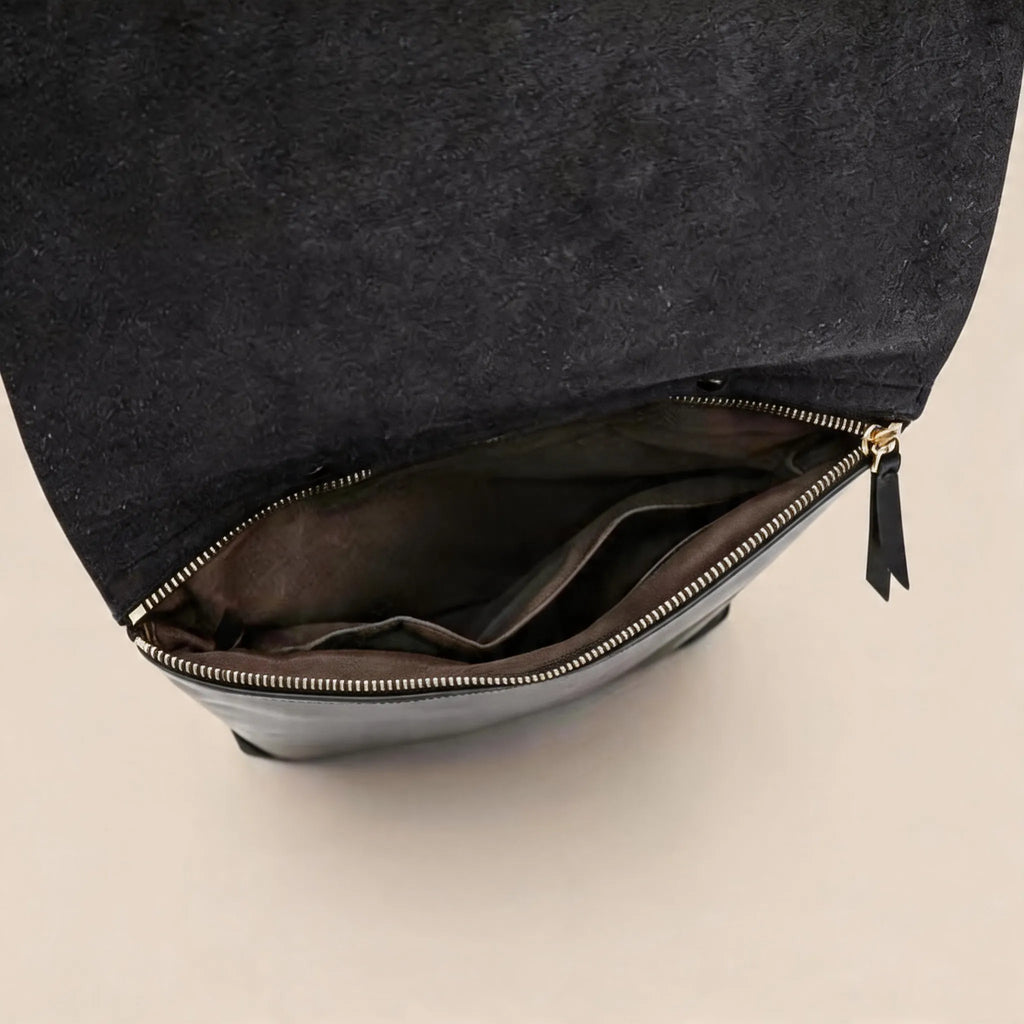 Black leather bag with gold zipper on a beige background