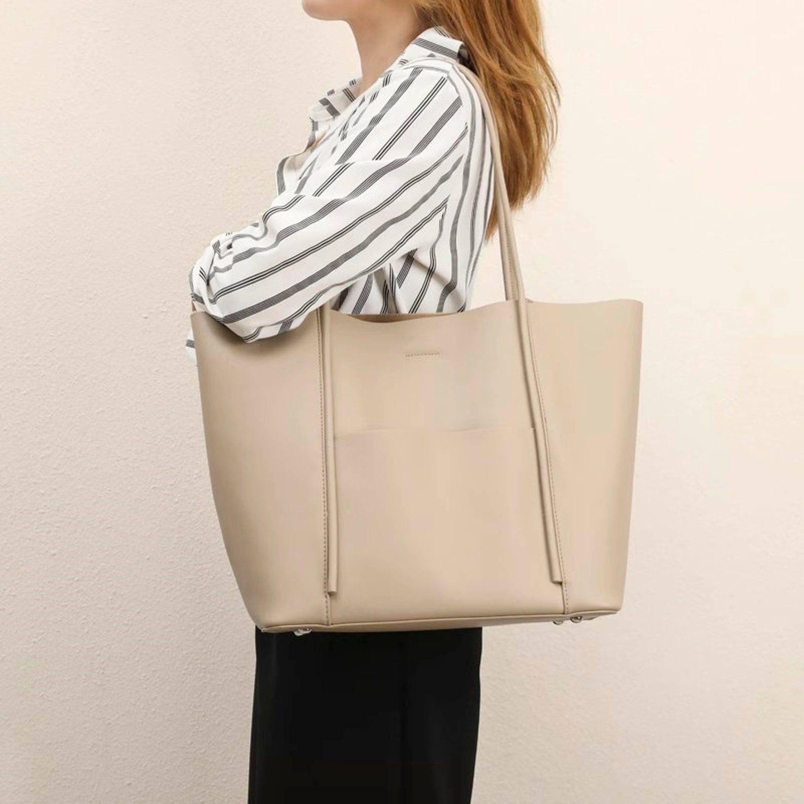 A person holding a large beige genuine leather tote bag with dual handles.