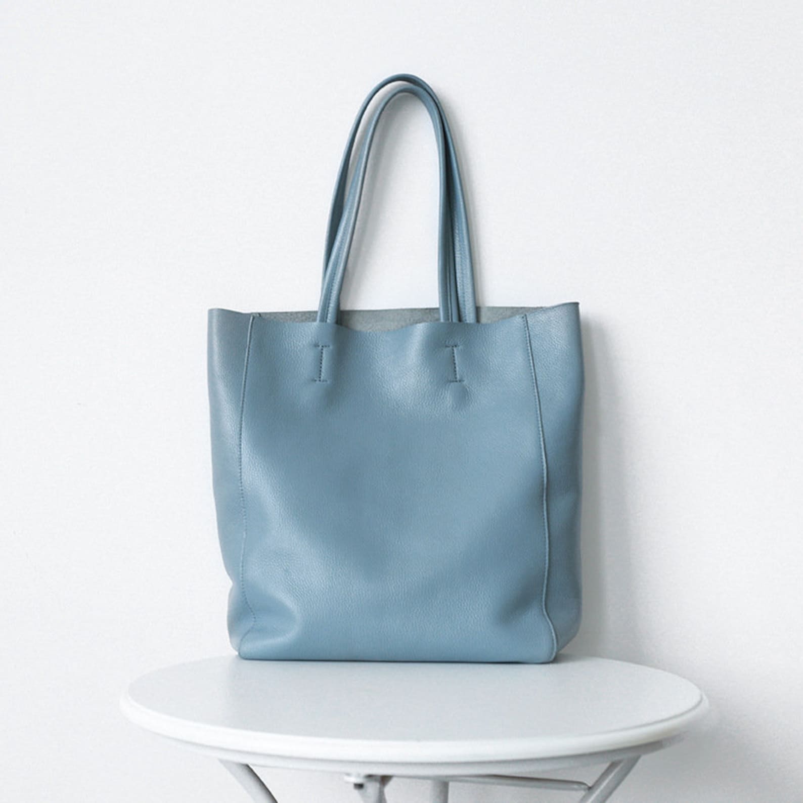 A sky blue leather tote bag placed on a white round table against a white background.