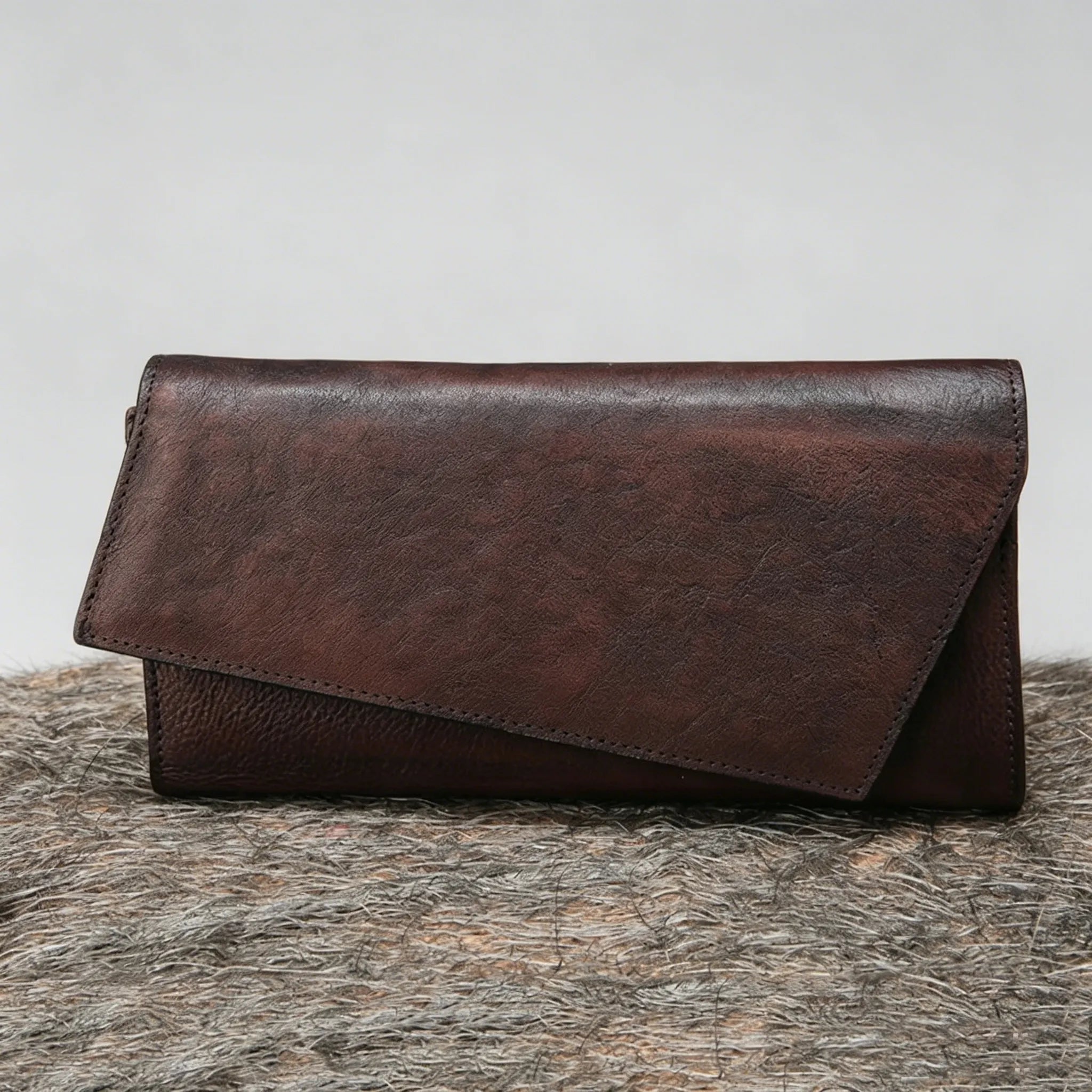 Brown leather clutch on a textured surface with a light gray background