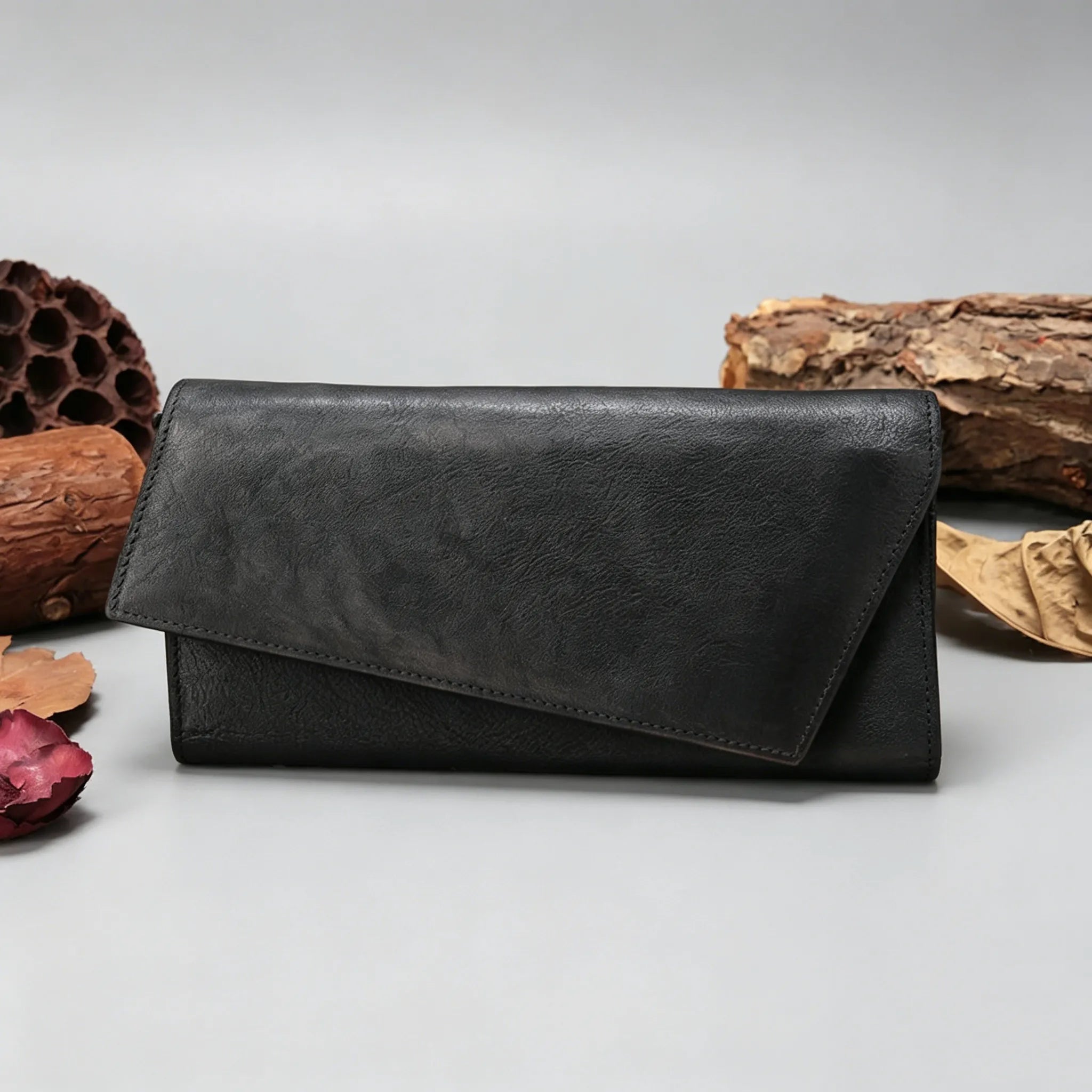 Black leather wallet on a light gray surface with natural elements in the background