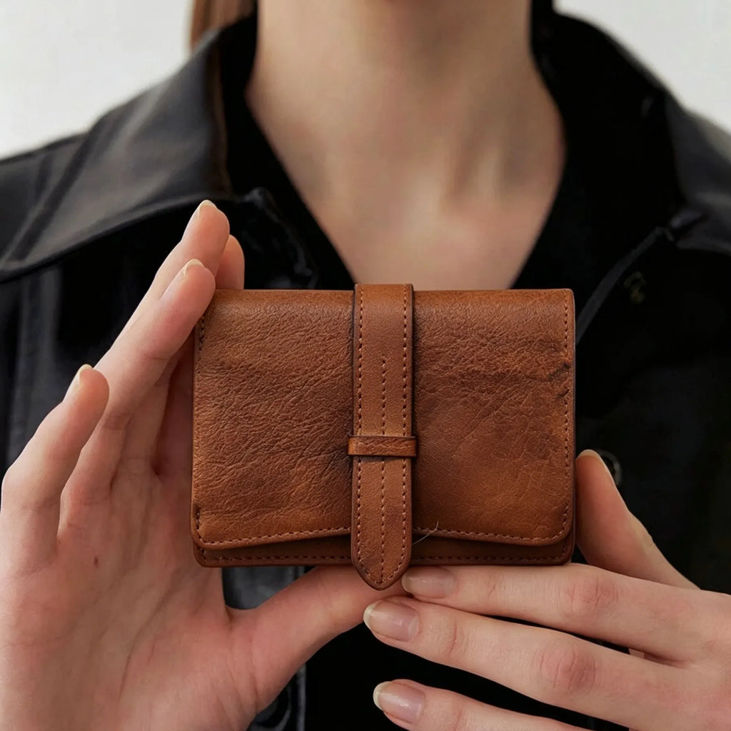 Brown leather wallet held by hands against a neutral background