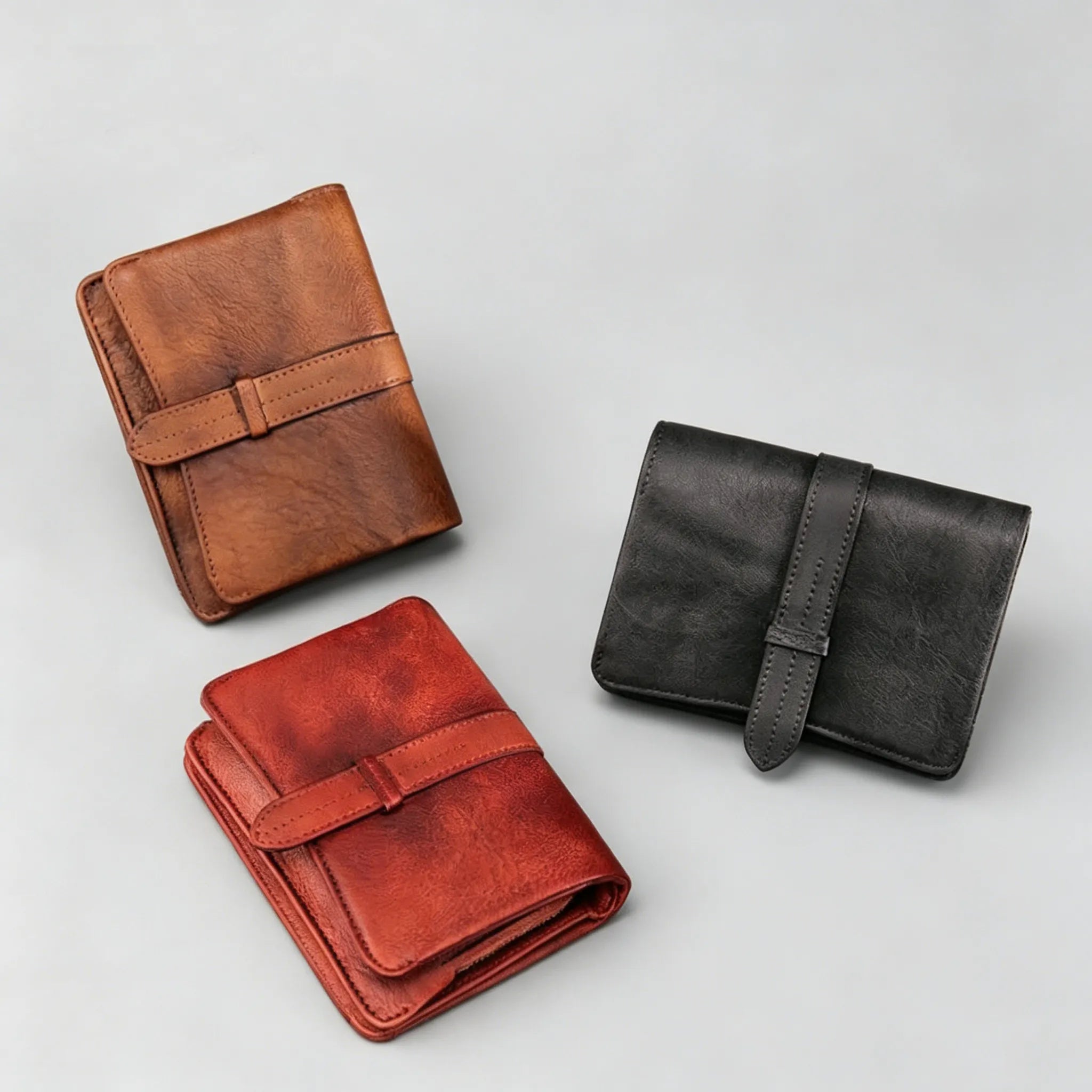Three leather wallets in brown, red, and black on a light gray background