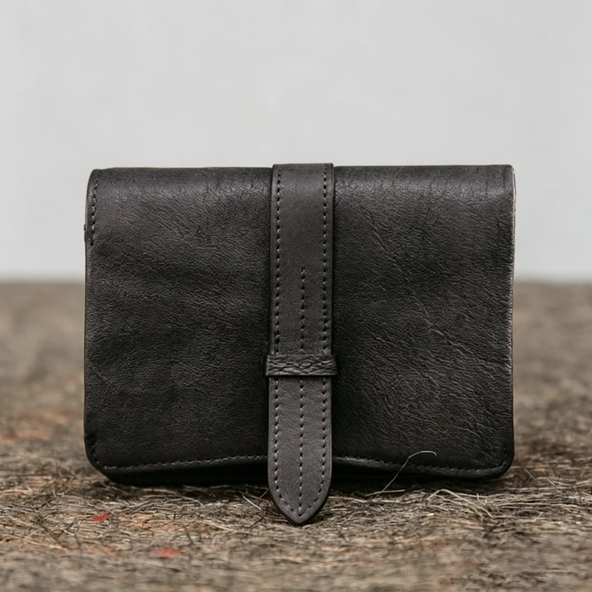 Black leather wallet with a strap on a textured surface