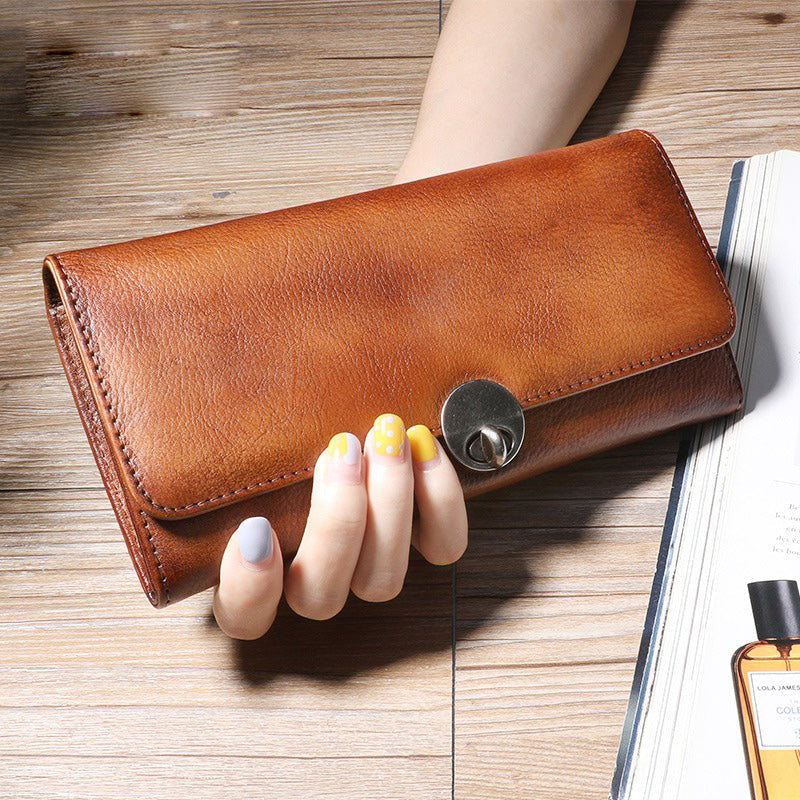 Brown leather wallet held by a hand with colorful nails on a wooden surface.