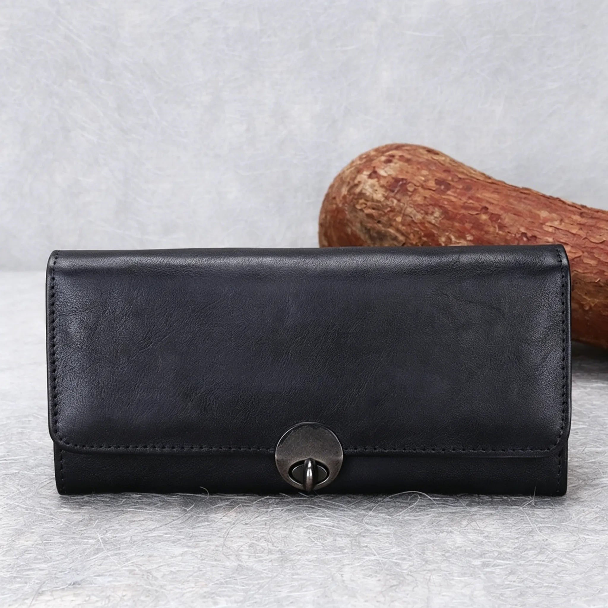 Black leather wallet with a metal clasp on a textured gray surface.