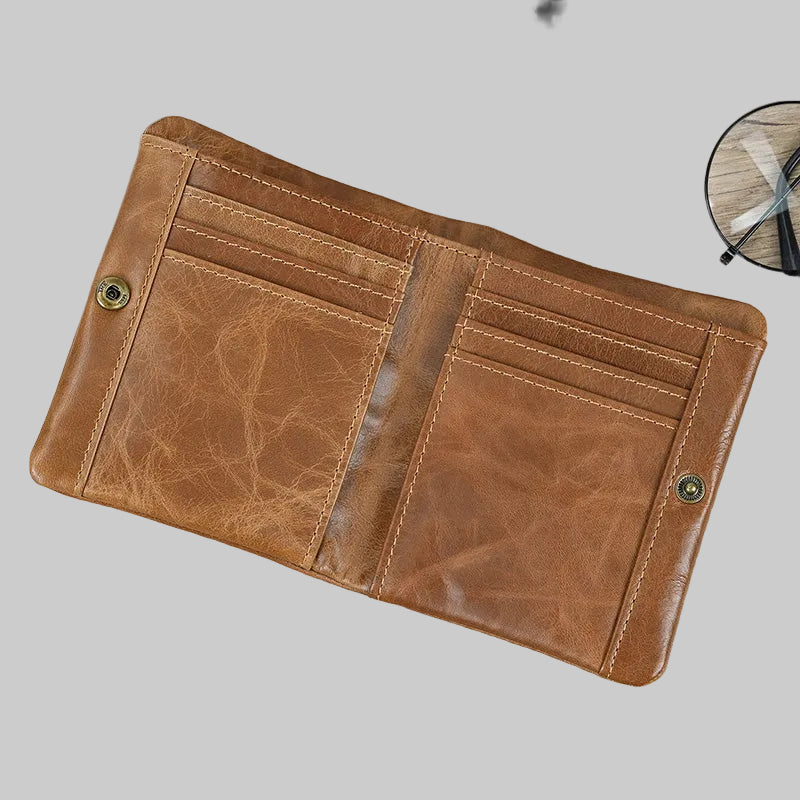 Brown leather wallet on a wooden surface with a phone and glasses in the background