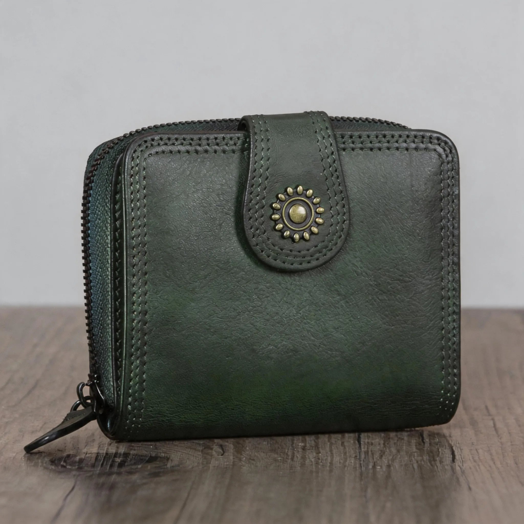 Green leather wallet with decorative clasp on a wooden surface