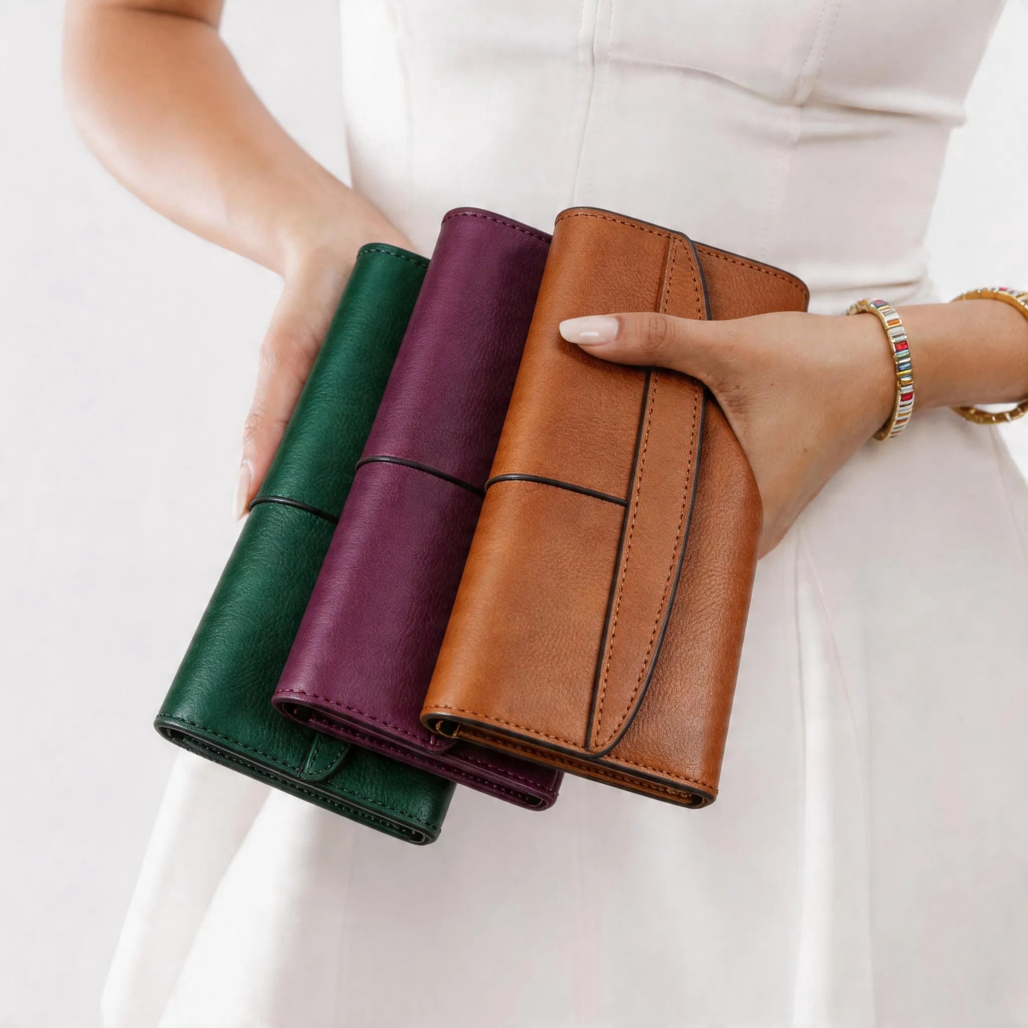 Three leather wallets in green, purple, and brown held by a person against a white background.