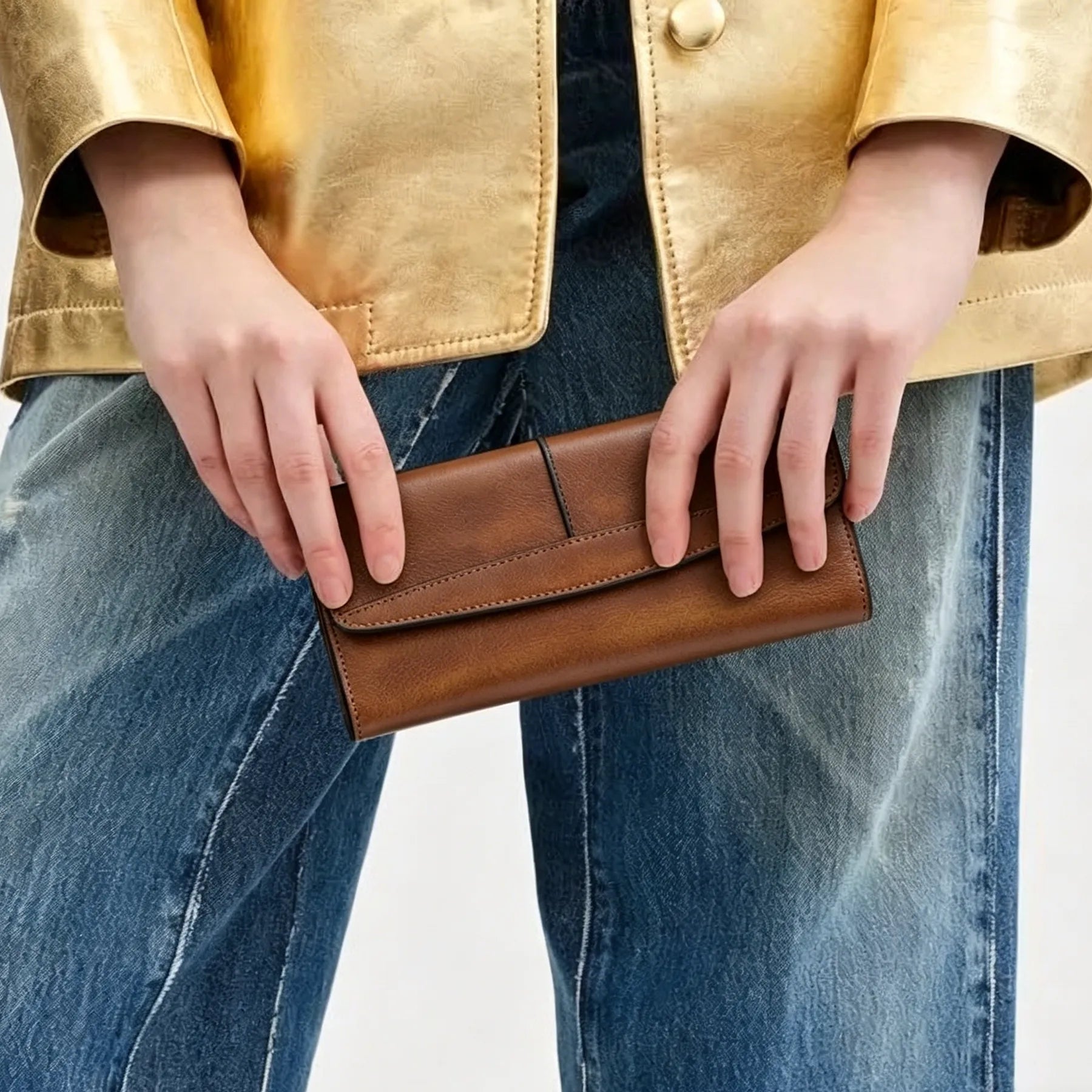 Person holding a brown leather wallet with a gold jacket and blue jeans on a white background