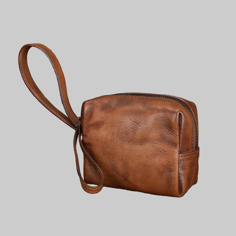 Brown leather pouch with strap on a textured surface