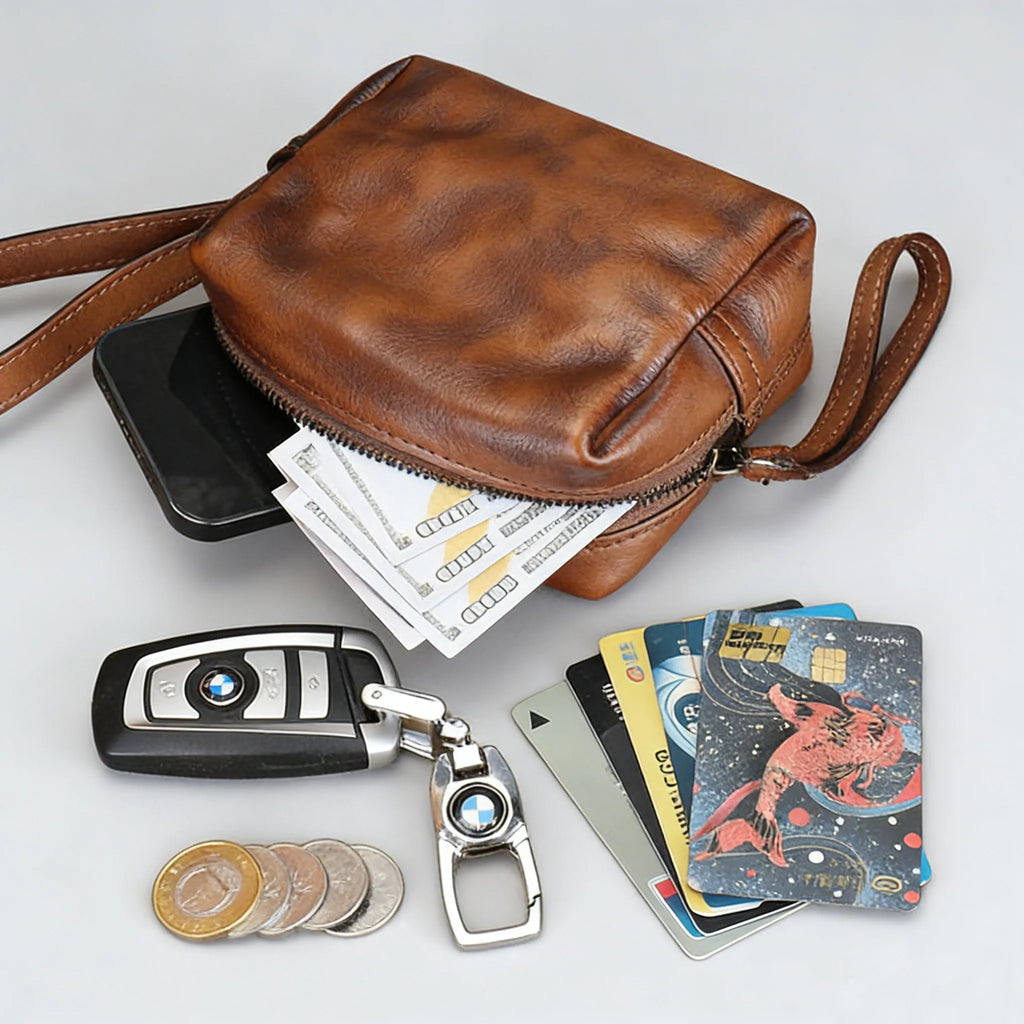 Brown leather crossbody bag with phone, money, keys, and cards on a light gray background