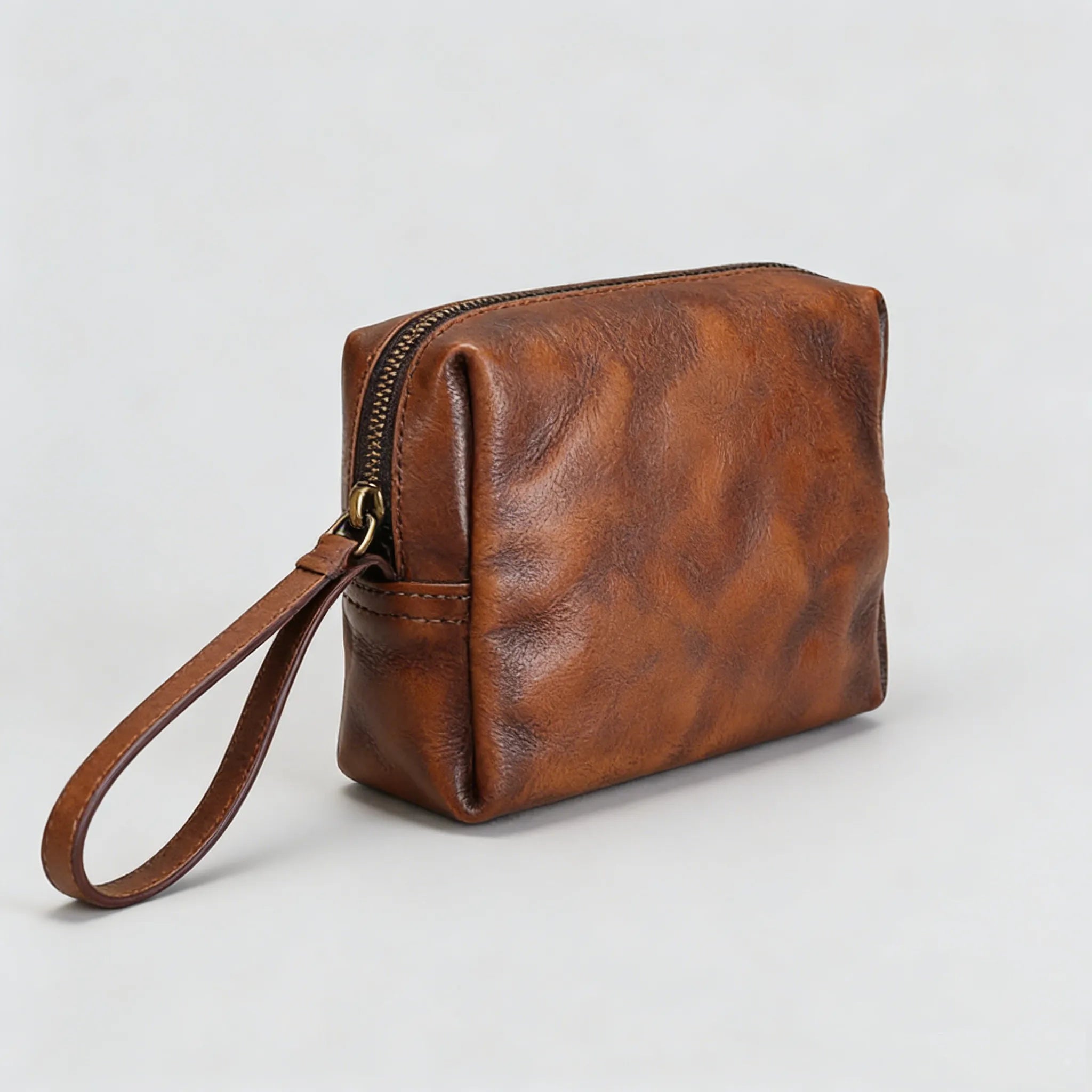 Brown leather clutch bag with a strap on a light gray background