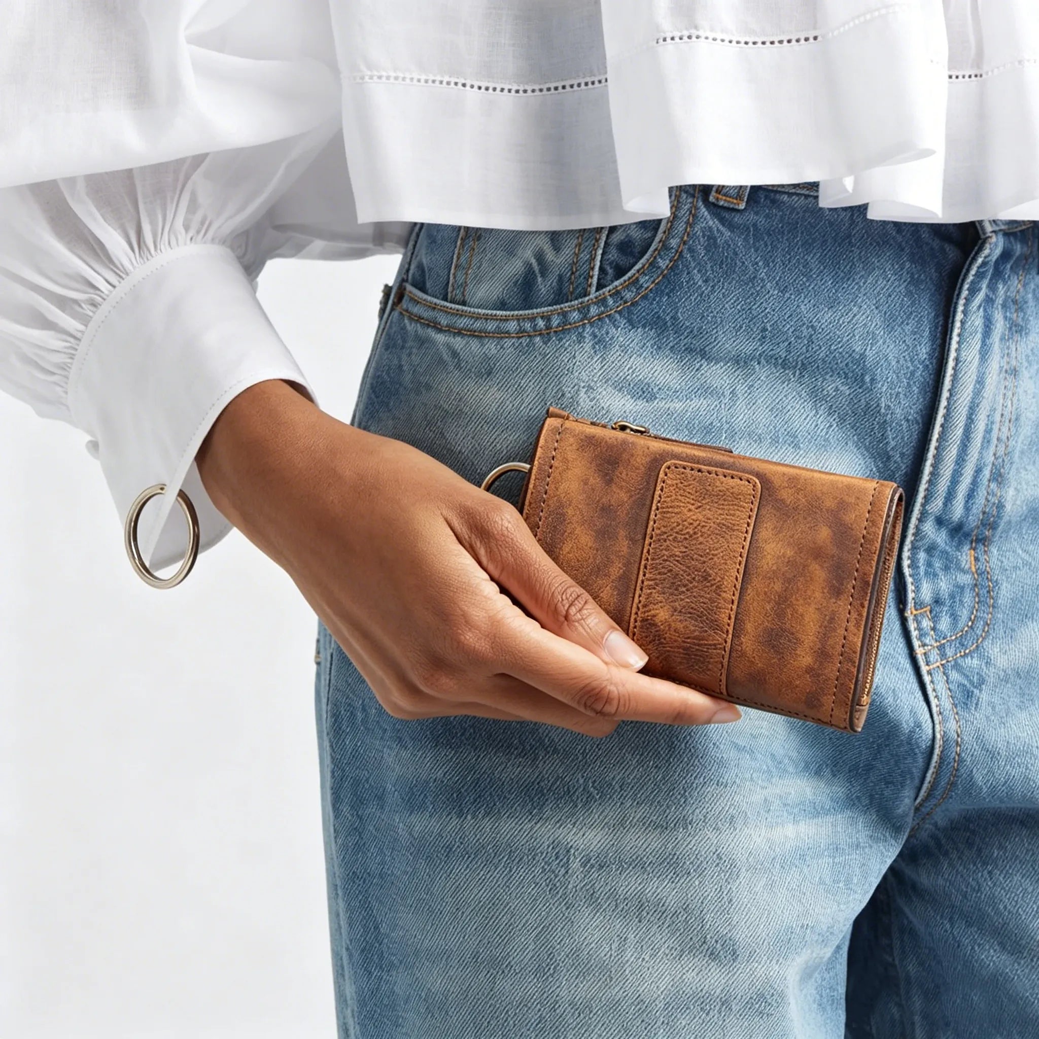 Person holding a brown wallet with a white shirt and blue jeans on a light gray background