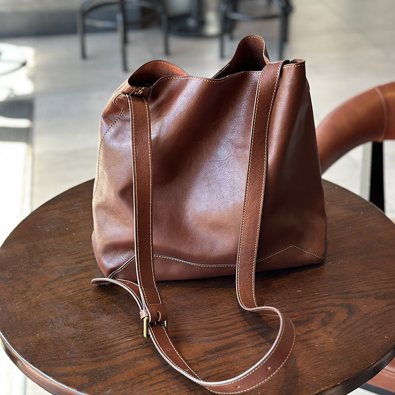 Brown leather bucket tote bag on a wooden table with a blurred indoor background