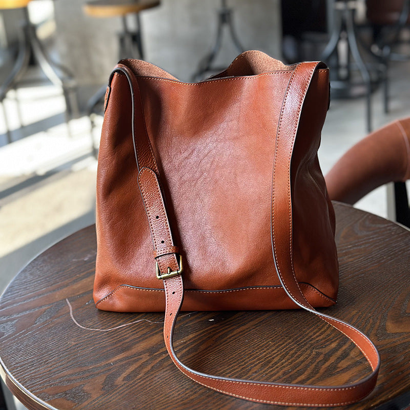 Brown leather bucket tote bag on a wooden table with a blurred indoor background