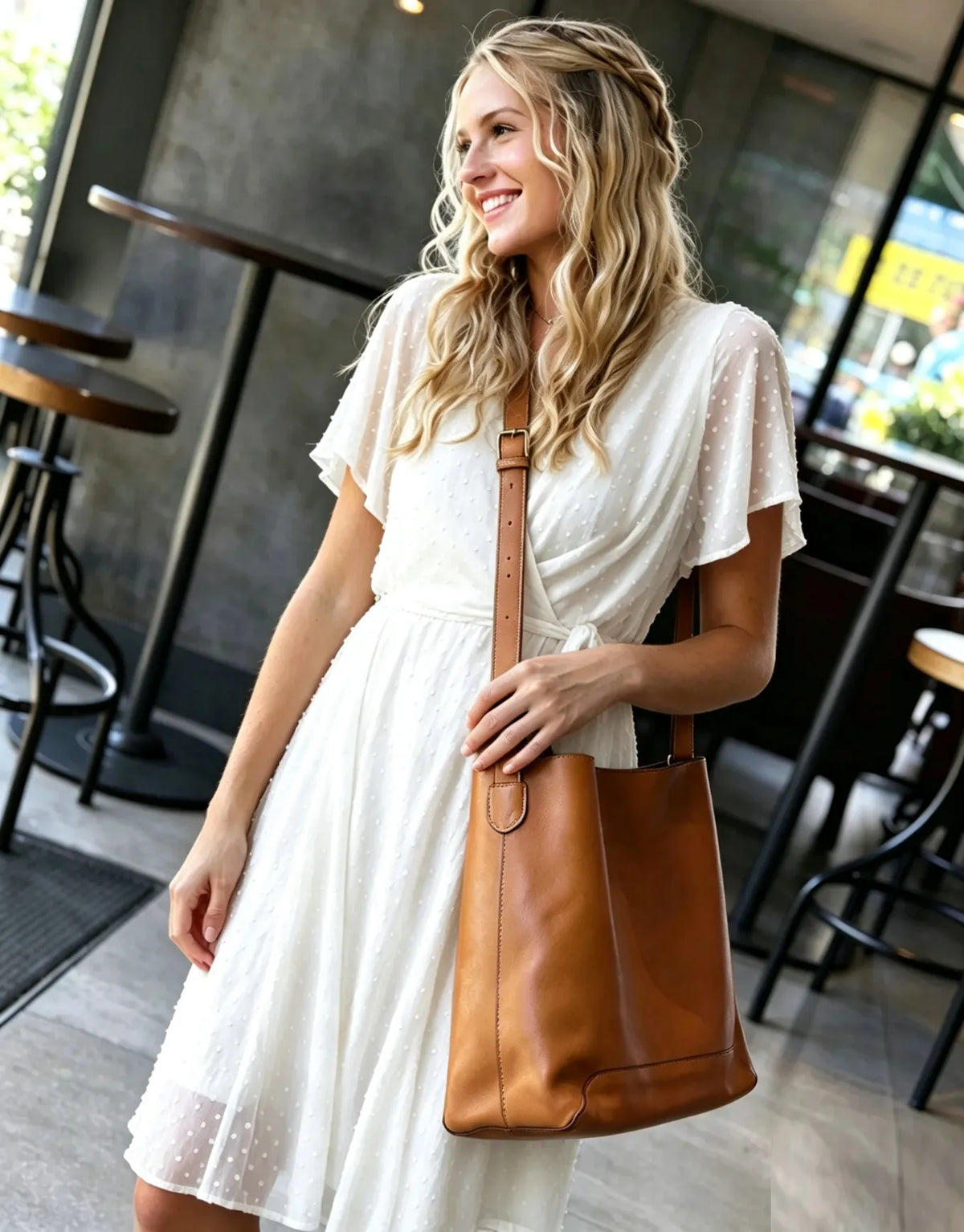 A woman in a white dress carrying a large brown leather shoulder bag in a cafe setting.