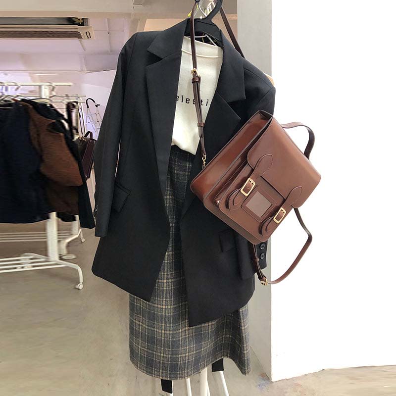 Black blazer, plaid skirt, and brown bag on a mannequin in a store setting.