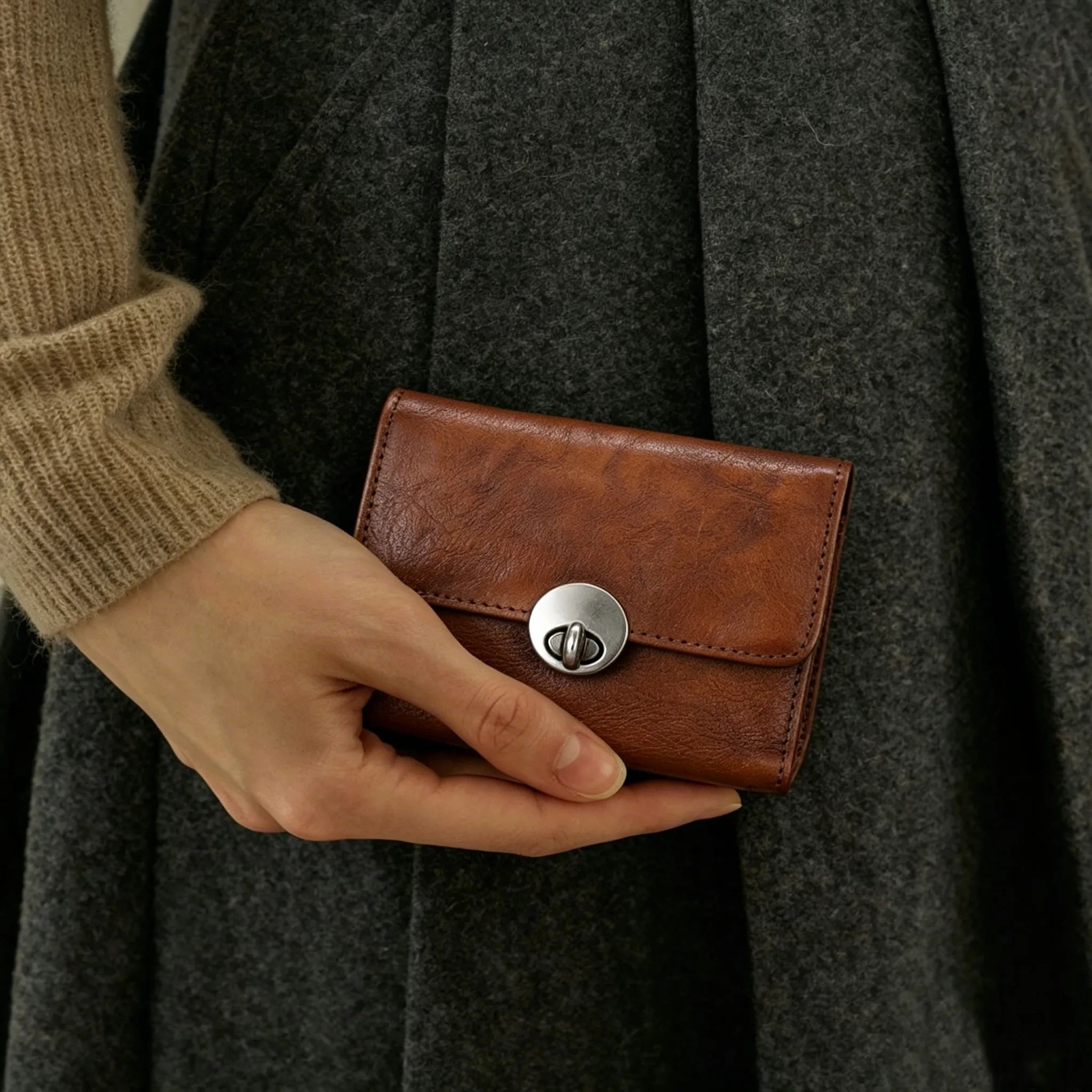 Person holding a brown leather wallet with a dark coat in the background