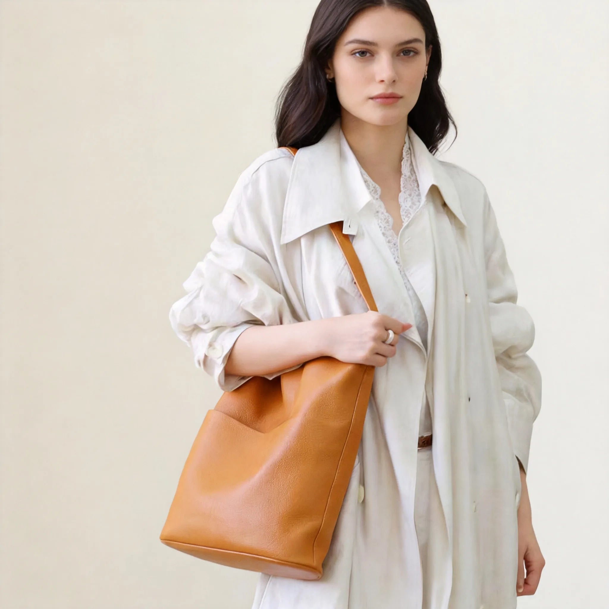 Woman holding a brown leather tote bag against a plain background