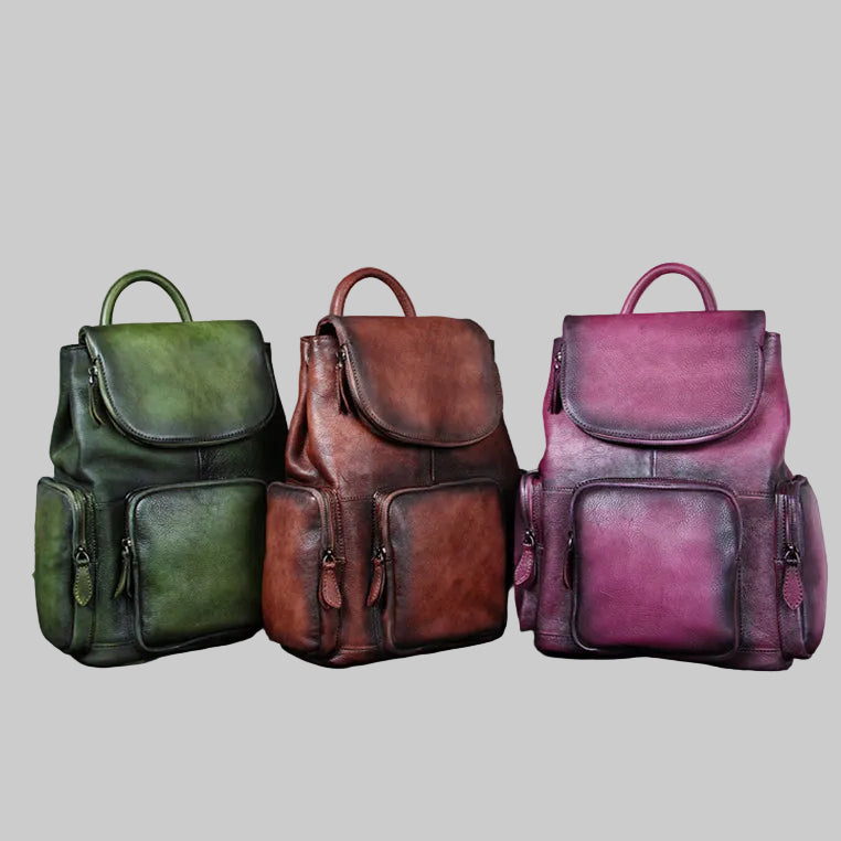 Three leather backpacks in green, brown, and purple on a gray background
