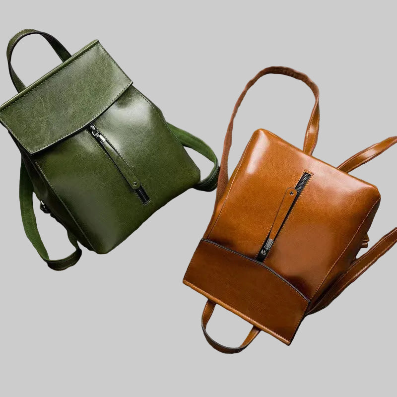 Green and brown leather backpacks on a gray surface with a magazine underneath.