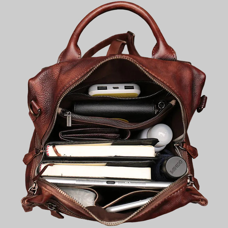 Brown leather backpack with compartments containing electronic devices on a gray background