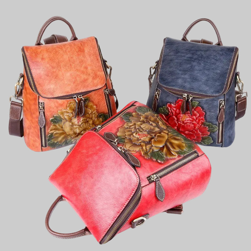 Three faux leather backpack-style handbags with floral embroidery, shown in orange, blue, and red on a solid gray background.