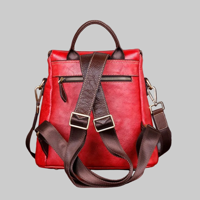 A red faux-leather backpack with dark brown straps, handles, and trim, featuring a top zipper and adjustable buckle straps, shown against a solid gray background.