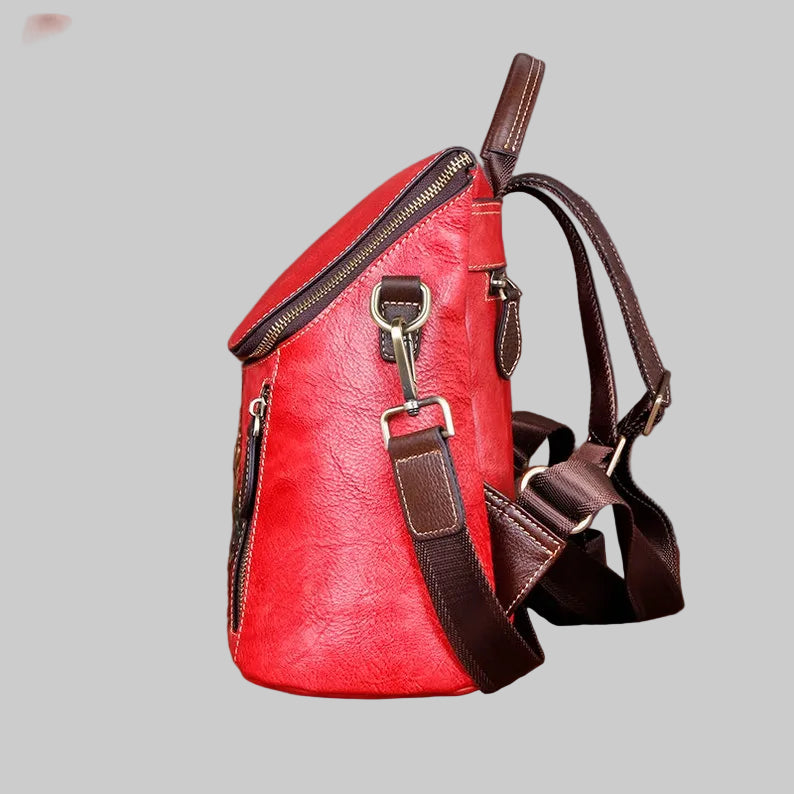 A red faux-leather backpack with dark brown straps, zippers, and trim, shown against a solid gray background.