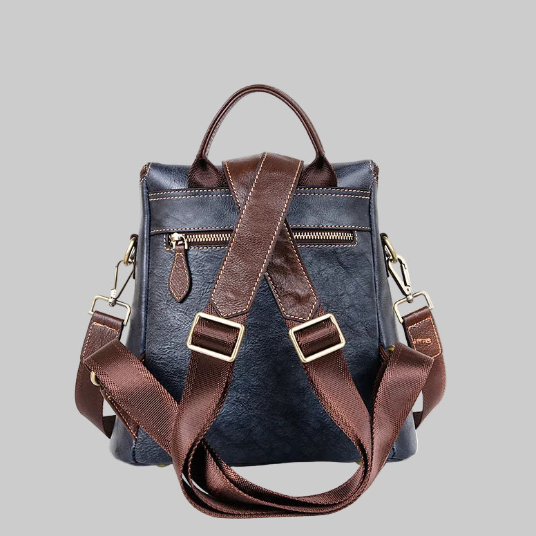A dark blue textured leather backpack with brown leather straps, handles, and buckles, shown from the back against a solid gray background.